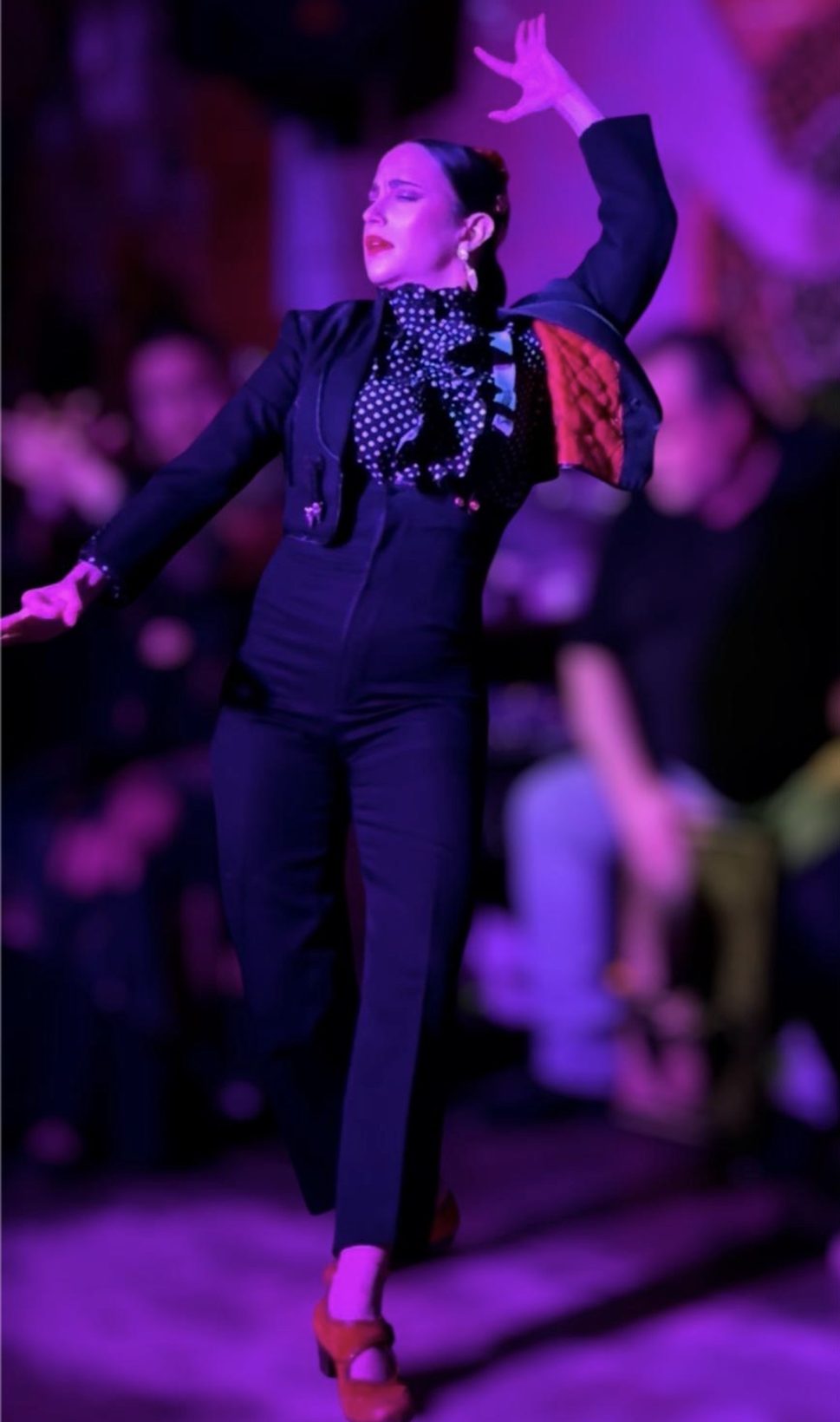 Bailaora del tablao flamenco Valencia El Toro y la Luna con chaqueta corta y zapatos rojos, con un brazo en alto sobre el escenario